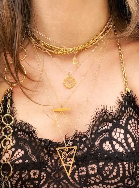 Model wears a black lace top, the gold Rael Cohen Fibonacci necklace, gold equation pendant, and gold chakra necklace.